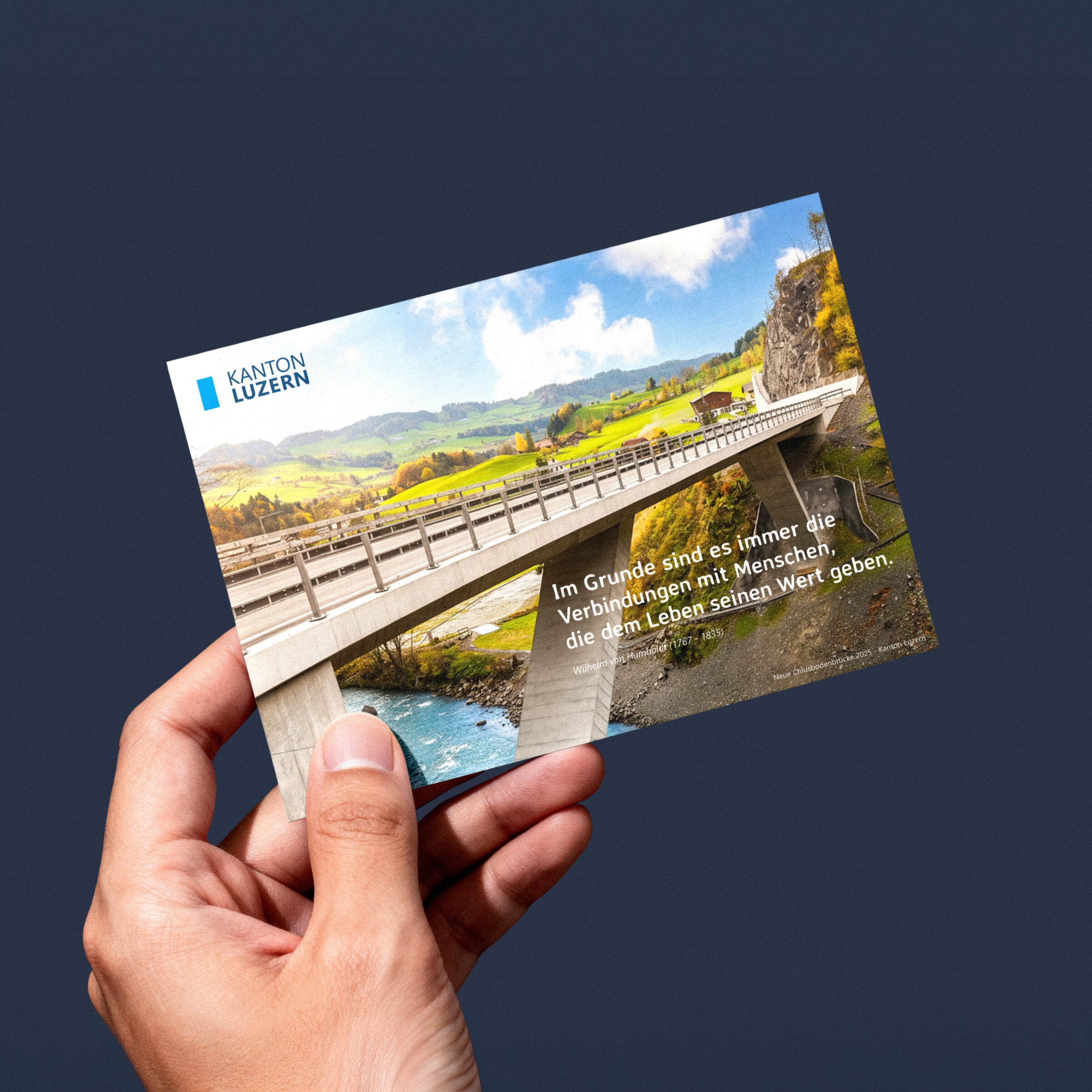 hand hält eine postkarte des kantons luzern mit einer brücke über einen fluss